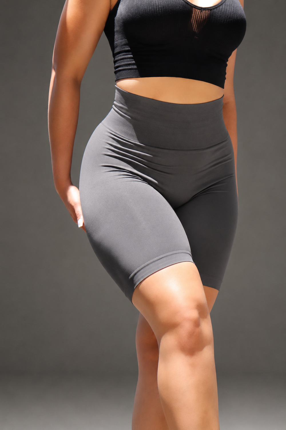 Person wearing black sports bra and gray shorts on a dark background